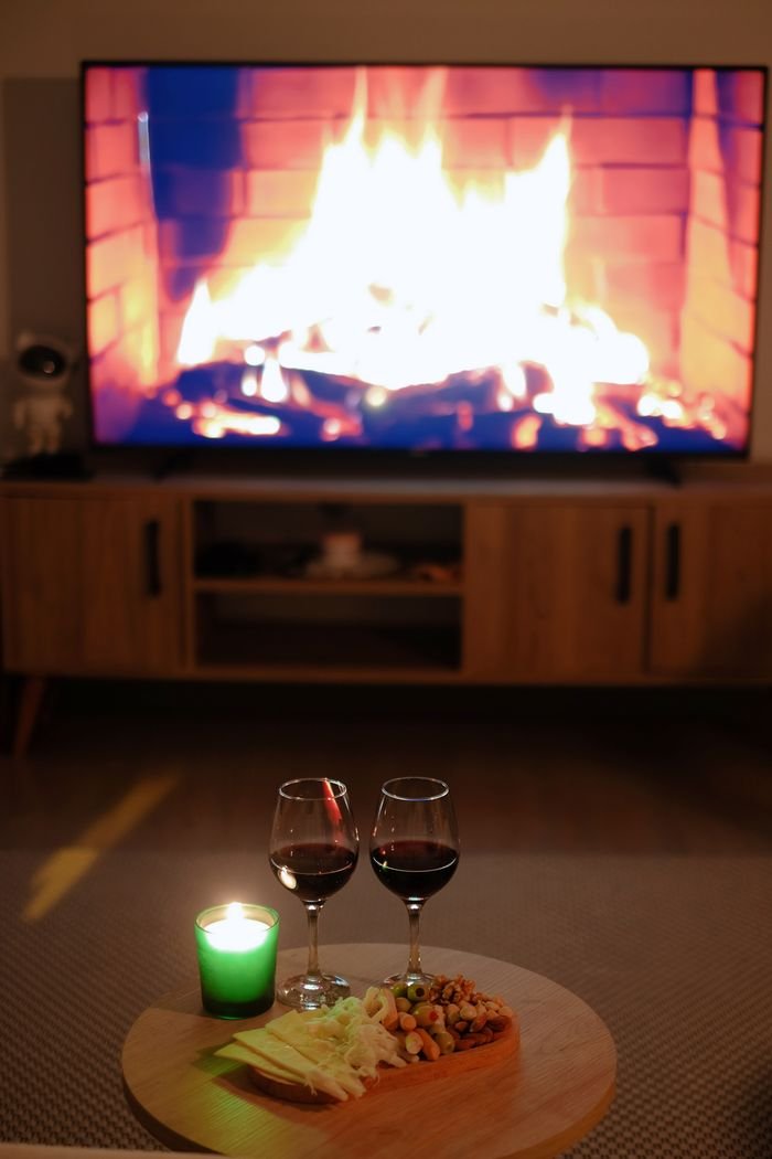 A cozy indoor setting featuring wine glasses and a fireplace on TV, perfect for relaxation.