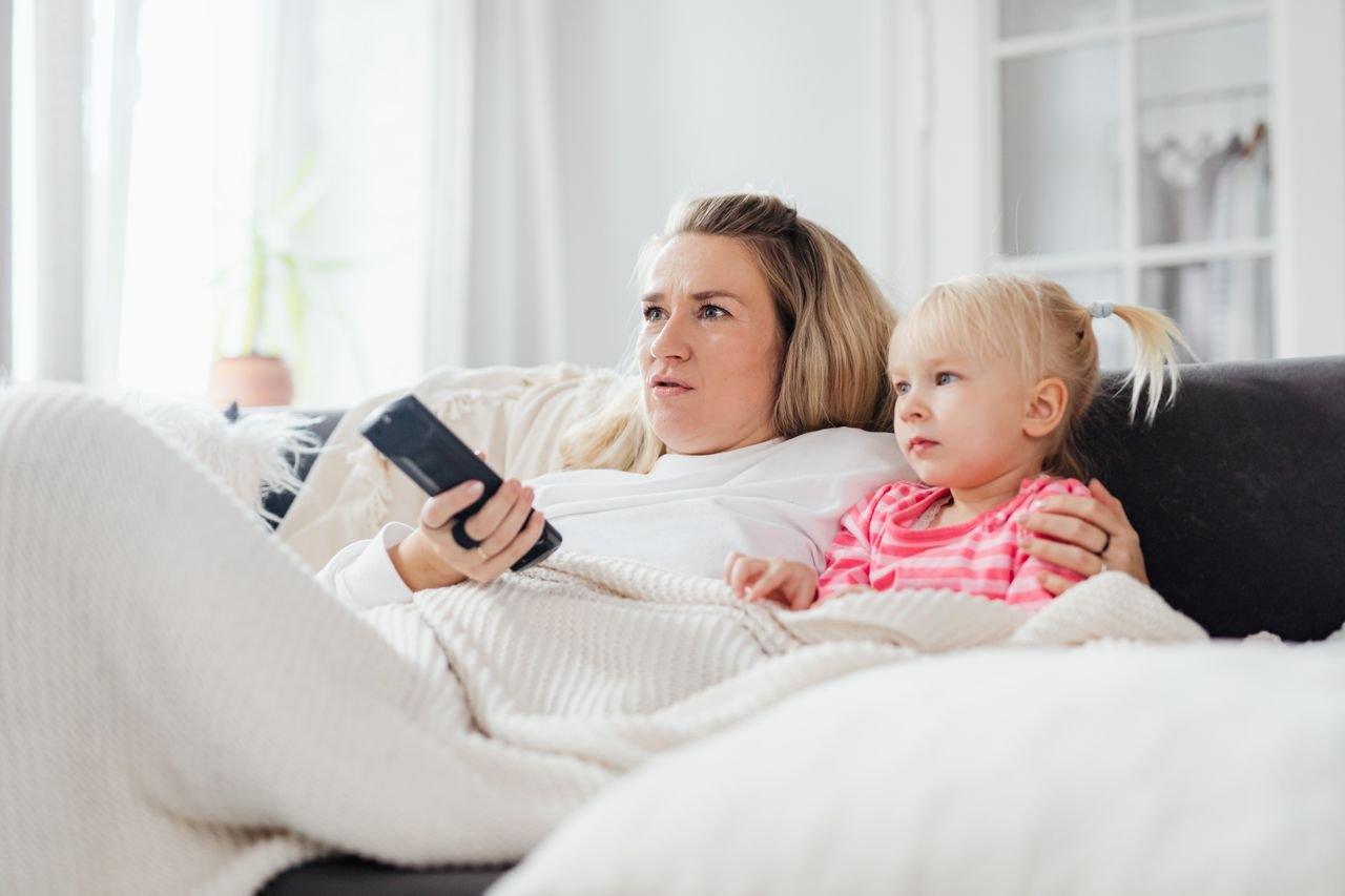 About A mother and daughter enjoying a relaxing time on the sofa, watching TV together indoors.